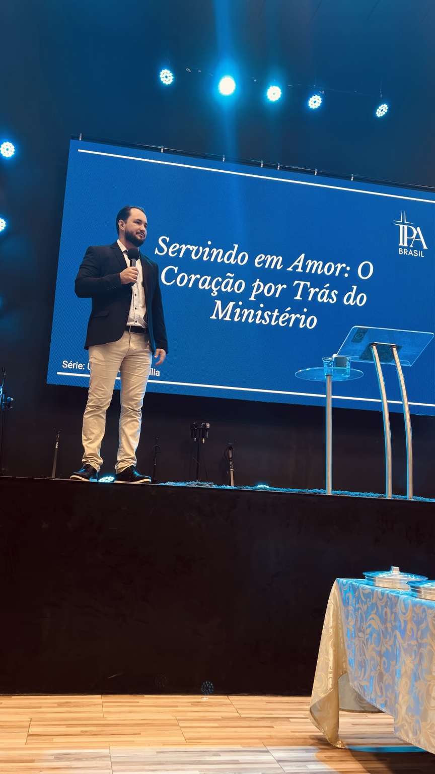 Pr. Marcelo Travagini ensinando no palco diante do painel Servindo em Amor
